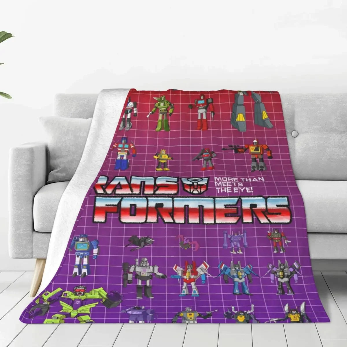 Couverture Transformers avec personnages robots colorés sur fond violet quadrillé, posée sur un canapé – Transformers.