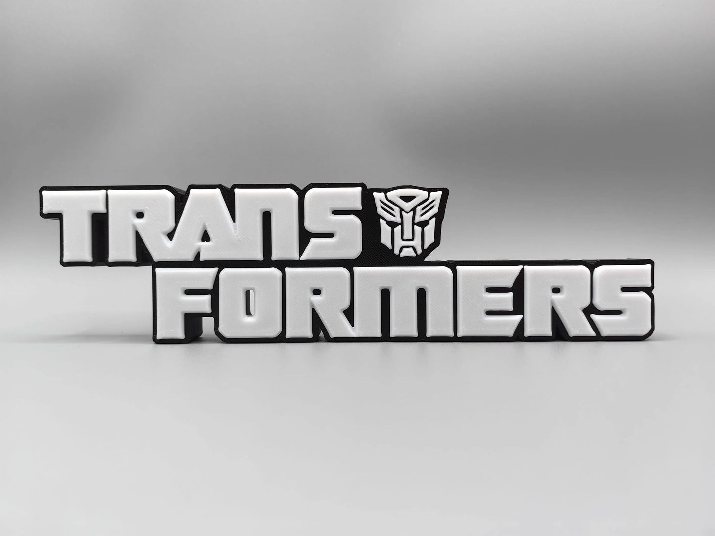 Transformers-plaat met monochroom zilverkleurig logo — gemetalliseerde bureauversiering