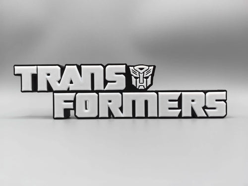 Transformers-plaat met monochroom zilverkleurig logo — gemetalliseerde bureauversiering