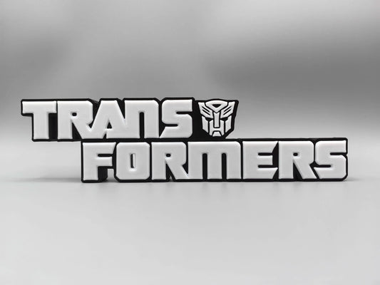 Transformers-plaat met monochroom zilverkleurig logo — gemetalliseerde bureauversiering